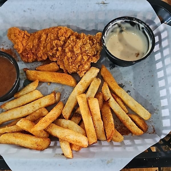 Crispy fried chicken tenders and seasoned fries served on a paper-lined tray with brown and creamy dipping sauces.