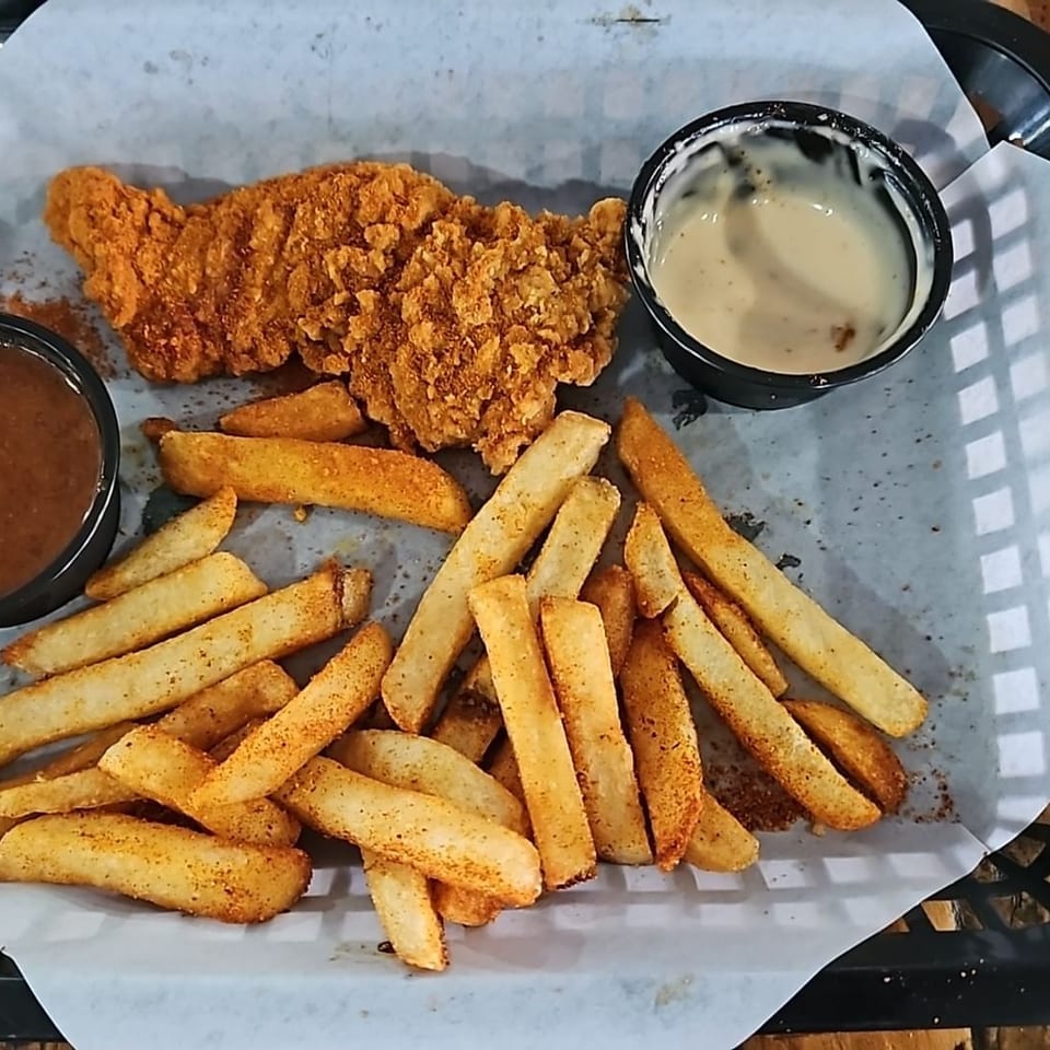 Crispy fried chicken tenders and seasoned fries served on a paper-lined tray with brown and creamy dipping sauces.