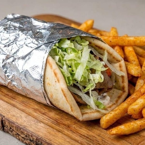 Foil-wrapped gyro filled with lettuce and meat, served with seasoned fries on a rustic wooden board.