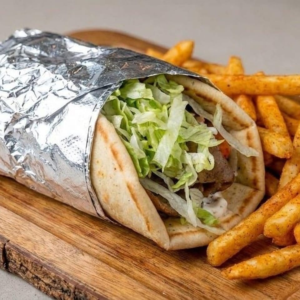 Foil-wrapped gyro filled with lettuce and meat, served with seasoned fries on a rustic wooden board.