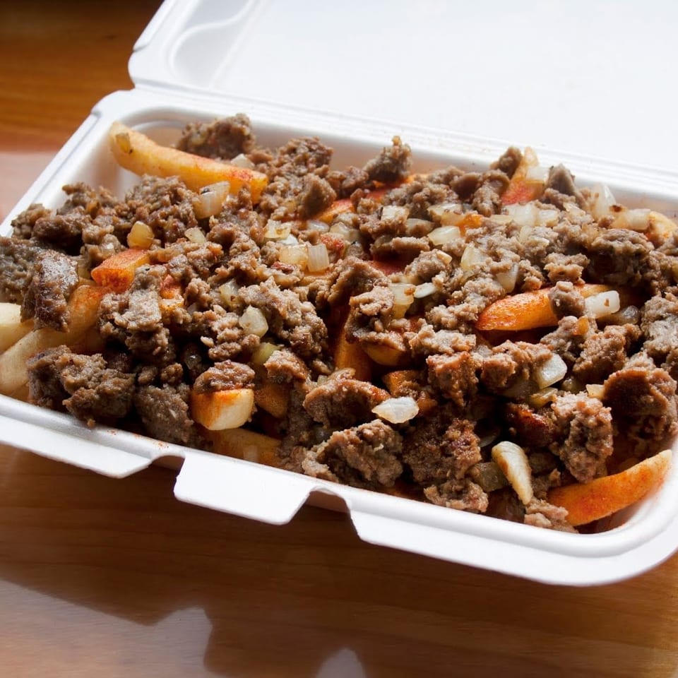 Takeout container filled with seasoned ground meat, fries, and chopped onions on a wooden table.